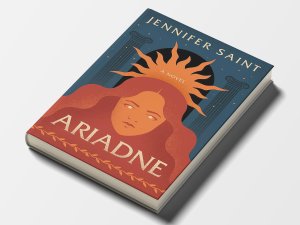 The cover of “Ariadne” by Jennifer Saint with a front view of a woman’s face. A sunburst comes from behind her head, while the background features two columns and an arched black doorway. The cover of “Ariadne” by Jennifer Saint with a front view of a woman’s face. A sunburst comes from behind her head, while the background features two columns and an arched black doorway.