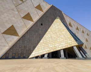 The front entrance of the Grand Egyptian Museum, featuring a triangular, pyramid-inspired entryway surrounded by a wall of hieroglyphs. The front entrance of the Grand Egyptian Museum, featuring a triangular, pyramid-inspired entryway surrounded by a wall of hieroglyphs.
