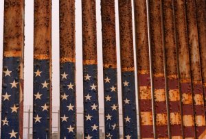 Image of a rusty section of the US/Mexico border wall with a facing American flag painted on it Image of a rusty section of the US/Mexico border wall with a facing American flag painted on it