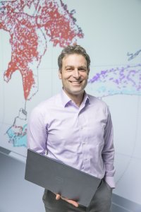 Photo of Dr. Hoffman holding a laptop in front of a map of the Great Lakes made of data points