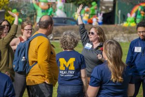 Small group of people gathering outside on a sunny day to listen to a speaker.