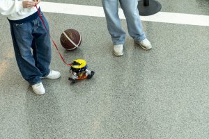 Two students stand next to a Ballbot, with its basketball sitting next to the robot.