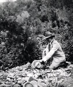 A black and white photograph of James Marshall Plumer outdoors with pottery on the ground
