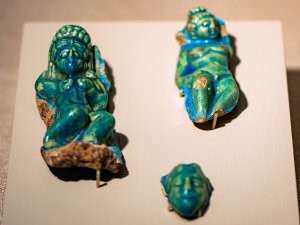 Three faience figurines on display at the Kelsey Museum: a reclining nude Aphrodite, Hermaphroditus lying naked, and a face.