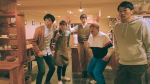Five young Japanese adults stand next to each other in a kitchen looking shocked