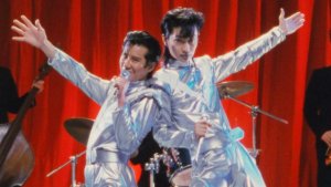 A film still showing two Japanese men in flashy silver outfits performing music onstage