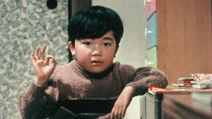 A film still of a young Japanese boy making the "ok" sign in a 1950s-style room