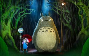 Image from a live version of My Neighbor Totoro showing a young woman at a bus stop next to a towering Totoro