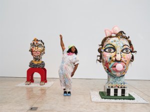 Image of venessa german, an African-American woman, standing with her right arm raised between two large sculptures