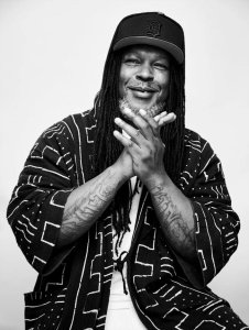 Shaka Senghor - an African-American man with long braids and a beard - smiles, clasping his hands