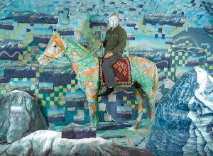 An image of a hooded man on a horse - the animal and background are covered with colorful patterns in blue and green, with hints of orange