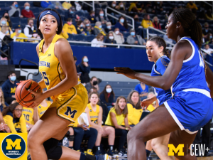 A female athlete in a yellow uniform dribbles a basketball at a University of Michigan women's basketball game.