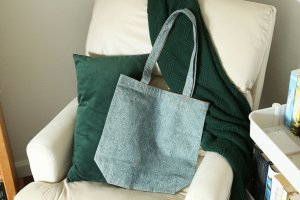An aqua-colored tote bag rests on a white arm chair and green pillow.