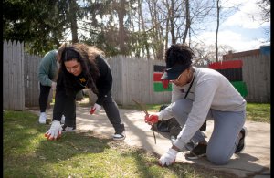 Two young adults displayed working on a project on their hands and knees. The weather looks sunny and calm.