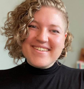 Photo of Hanna Barton smiling wearing a black shirt and short curly blonde hair