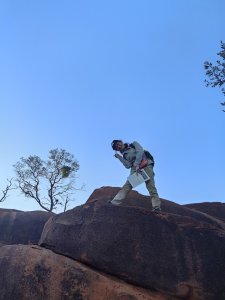 A woman smiles for the camera while standing on top of a large boulder