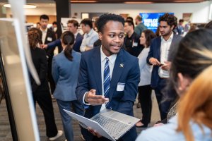 Person in blue suit holds laptop and presents poster
