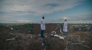 2 men standing in front of a crater and debris.