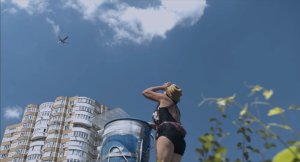 Woman looking up at the sky with a building in the background and a plane flying above.