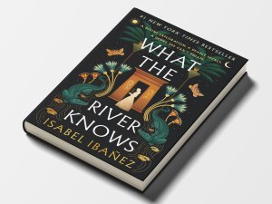 The cover of “What the River Knows” by Isabel Ibañez, with an illustration of a woman standing under an archway surrounded by palm trees, plants, and crocodiles.