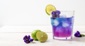 Layered purple and blue drink in a glass with ice, garnished with lime and a purple flower.