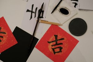 Chinese calligraphy brushes, ink, and red paper with the character for luck or auspiciousness