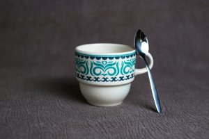 White and blue teacup with a silver spoon rested on it.