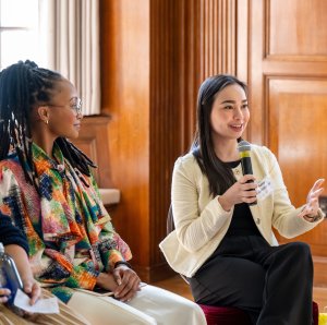 Two UM-BLI alumni sitting. Person to the right is speaking on a microphone and person to the left is listening.