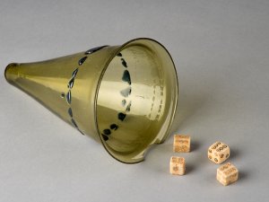 Conical green lamp with a row of black dots encircling it. The object has been repurposed as a dice cup; four bone dice with concentric circle pips sit near it.
