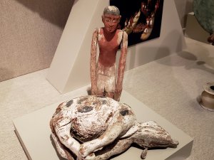 Kelsey Museum case showing wooden, painted figurines of a man kneeling next to a butchered cow.