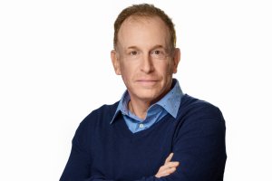 A man smiles for the camera in front of a white background