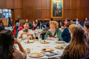 Students sitting at a round table sharing a meal and laughing together.