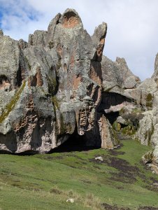 Large rocky outcrop with a rockshelter at the bottom behind a grassy field