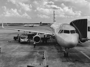 B&W photo of airplane on tarmac with disembarking canopy on right.