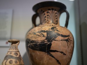 Close-up of two pottery vessels on display: a two-handled amphora with a black silhouette of a bearded centaur, and the upper portion of an alabastron with registers of animals.
