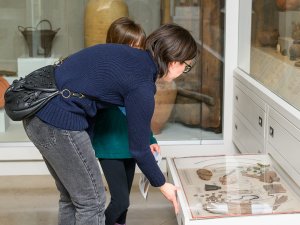A parent and child look into a display drawer containing coins, musical instruments, figurines, and other objects of everyday life from the ancient town of Karanis, Egypt.
