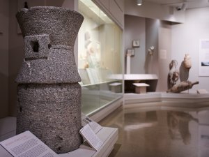 View of the Kelsey Museum’s Roman galleries. A large stone grain mill is visible in the foreground, while the background features mineral-encrusted amphorae and smaller objects on display behind glass.