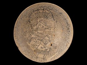 Buff clay incantation bowl with drawings of two humanoid figures surrounded by writing.