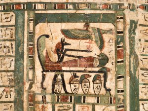 Close-up of a painted image found on the lid of the coffin of Djehutymose, showing the dog-headed Egyptian god Anubis mummifying the priest himself. A row of canopic jars rests at the god’s feet.