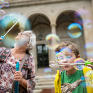 Adult and child blowing bubbles outside of the Clements Library.