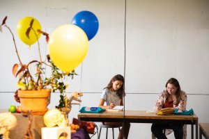 Students work on a still life featuring three maize and blue balloons at a table in a drawing studio.