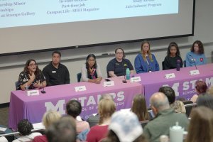 A group of Stamps staff and students at a long table engaged in a panel Q&amp;A session