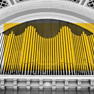Tall pipes highlighted in bright yellow form a wave pattern inside a grand, arched building.