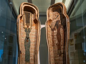View of the open coffin of Djehutymose, showing painted depictions of the ancient Egyptian goddesses Nut and Amentet standing, surrounded by rows of hieroglyphs. Nut has her hands and hair raised above her head, while Amentet walks in profile with a falcon on her head.