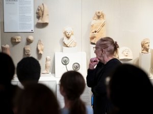 Display of anatomical votives and other Roman medical devices in the Kelsey Museum. A group of visitors and a docent examine the case.