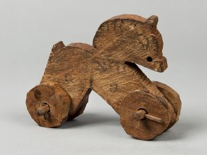 Ancient wheeled wooden horse toy with faint traces of paint visible on the mane and saddle.