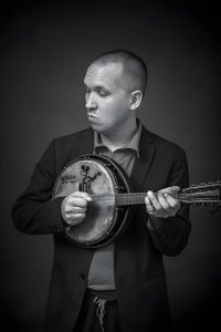 Black-and-white photo of the speaker-performer holding a banjo.