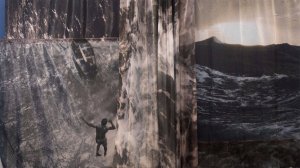 An abstract image of textured greys and browns, with the textures fading into photos of ocean waves. the silhouette of a black man jumping into the water is visible.