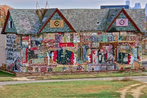 A colorful, two-story building covered in intricate mosaics, beads, vibrant artwork, and painted text.