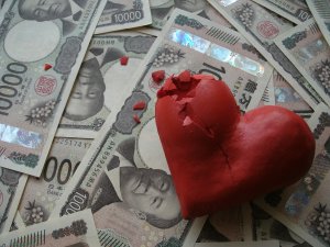 A photo of a pile of Japanese 10,000 yen bills with a 3-D clay-like red heart with some chips and cracks.